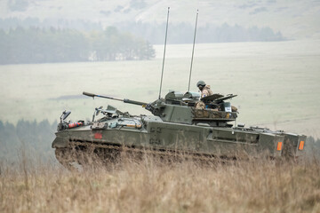 British army Warrior FV510 with commander in action, moving across countryside