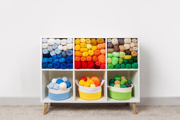 Shelving with storage baskets and colored balls of yarn for knitting. Bright yarn balls lined up on the shelves. Organizing and storage in craft room. Handmade, needle craft, creativity and  hobby.