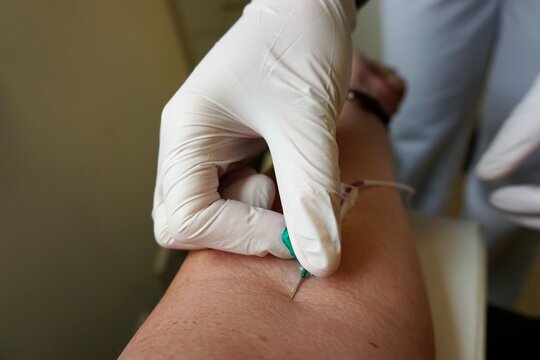 &Auml;rztin mit wei&szlig;en medizinischen Handschuhen setzt Infusionsnadel in Arm von Patientin zur Blutabnahme in Arztpraxis 