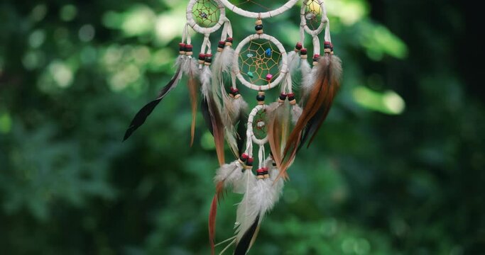 Feathers amulet Dream catcher with white feathers flying in wind at nature background. Hunter of dreams against green tree leaves. Close-up magical amulet Dream catcher