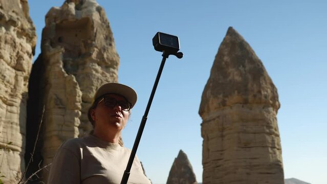 A girl blogger in glasses is recording a story on an action camera. Against the background of a sandstone rock in the form of phalos. Valley of Love in Cappadocia. Holidays in Turkey