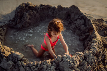 Little girl playing on the beach, digging hole in sand.