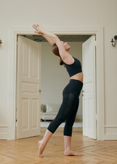 a woman does yoga at home performing an asana standing in a bright room