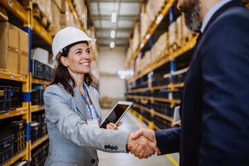 Managers in suits shaking hands in warehouse. - obrazy, fototapety, plakaty