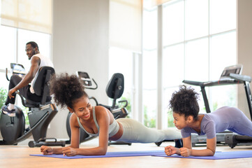 African American mother and daughter in sportswear practicing yoga together on yoga mat at the gym. Black family sporty fitness workout.
