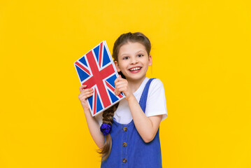 English for children. A little girl holds a textbook with an English flag in her hands. Children's...