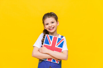 English courses for children.  A little girl holds a book with the flag of England and smiles broadly. Children's education. Language learning. Yellow isolated background.