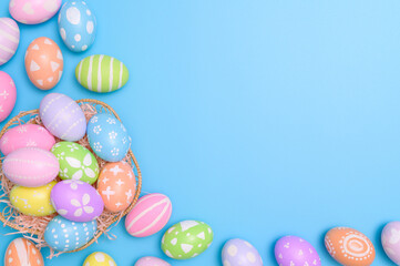 Fototapeta na wymiar Happy Easter holiday greeting card design concept. Colorful Easter Eggs and spring flowers on blue background. Flat lay, top view, copy space.