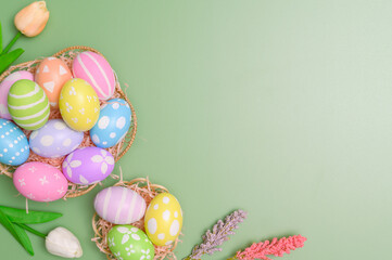 Fototapeta na wymiar Happy Easter holiday greeting card design concept. Colorful Easter Eggs and spring flowers on pastel green background. Flat lay, top view, copy space.