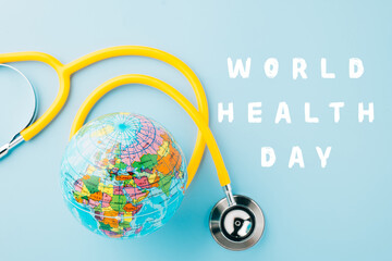 World Health Day. Yellow doctor stethoscope and world globe isolated on pastel blue background with copy space for text, Save world day, Green Earth Environment, Healthcare and medical concept