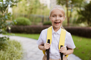 Schoolgirl back to school after summer vacations. Pupil in uniform smiling early morning outdoor. 