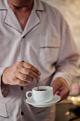 Senior man in pajamas mixing sugar in cup