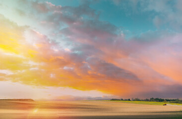 Obraz premium Bright Orange Yellow Cloudy Sky. Field At Sunset Sunrise. Tractor Plowing Field In Spring Season Sunny Day. Bright Clouds On Background. Countryside Rural Field Landscape. Agricultural Concept.