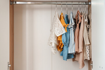 Children's clothes, girls' dresses hang on hangers in an open closet, dressing room