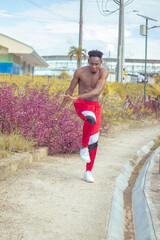 Obraz premium Joven afro bailando al estilo urbano sin camiseta, con hermosa vegetacion y cielo de fondo