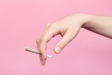 A woman's hand holds a joint with medical marijuana with her fingers.  On a pink background