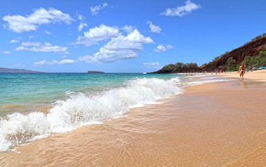 Gold sand beach walker. Blue sea water and dramatic clouds. Maui, Hawaii, USA. Unidentifiable sun bather.