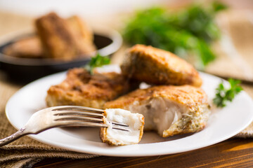 A piece of hake fish fried in a crispy crust, in a plate.