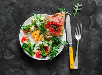 Healthy breakfast - fried egg with vegetables, arugula and salmon cottage cheese toast on a dark background, top view