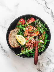 Delicious healthy diet salad with baked salmon, arugula and vegetables on a light marble background, top view