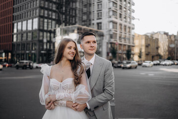 Fototapeta premium Close up portrait of bride and groom getting married, having photoshoot outdoors. Woman wearing wedding dress, kissing groom, man looking at camera. Concept of marriage and love.