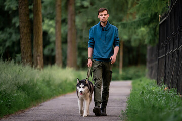 A cute young man is walking along the road with his beloved Siberian Husky dog in nature. © Maria Moroz