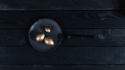 Obraz premium Golden eggs with black fork on black plate on dark background. Easter concept