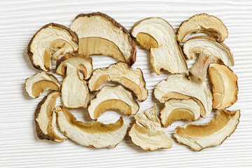 Dry slices of porcini as gourmet food ingredient, white wooden table, texture background from forest boletus mushrooms, top view, flat lay, aesthetic pattern. Vegetable organic protein food