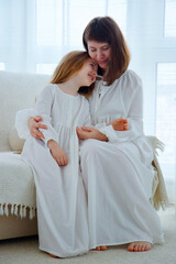 Young mother and little cute daughter in old fashioned white pajamas at home in the morning