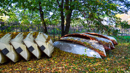 
Pleasure boats are pulled out of the pond and stacked under a tree to prepare for winter. The boats lie on the grass and are strewn with autumn leaves.