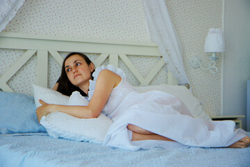 Portrait of young woman in retro-styled nightdress lies on the bed in the bedroom at home