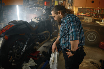 Brutal biker wiping his hands while repairing motorcycle engine