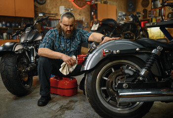 Fototapeta na wymiar Bearded mature man biker cleaning motorcycle in garage workstation