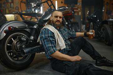 Fototapeta na wymiar Exhausted mature man biker sitting on floor holding opened glass of beer