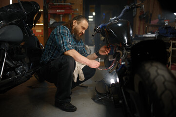 Fototapeta na wymiar Mature man biker repairing motorcycle in garage at evening