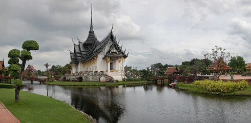 Panoramic photo of the architectural park of Oriental culture. Religious buildings of Thai history: palace and temple complexes. The exhibits are surrounded by ponds, tropical greenery and flowers
