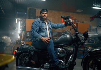 Fototapeta na wymiar Portrait of mature bearded biker on motorcycle over garage interior