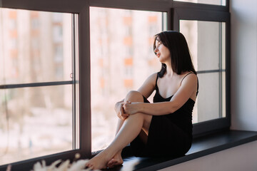 Fototapeta premium A girl with shoulder-length black hair is sitting by a huge window 4552.