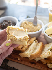 A woman holds a slice of bread with hummus. There are several appetizers on the table