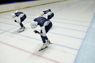 Three young sportsmen in sports uniform and skates bending forwards while sliding along ice rink...