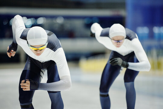 Two young male figure skaters in sports uniform moving forwards along ice rink while taking part in short track speed skating competition