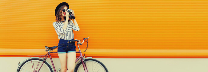 Summer image of happy smiling young woman photographer taking picture by film camera with bicycle...