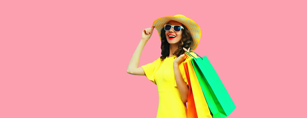 Portrait of beautiful happy smiling young woman with shopping bags wearing yellow dress and summer straw hat on pink background