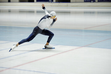 Fototapeta premium Side view of young active man in sports uniform and eyeglasses having short track speed skating training while sliding on ice inside arena