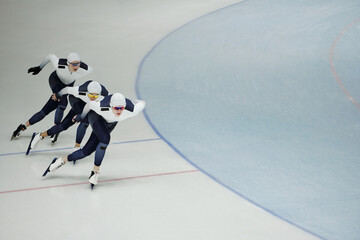 Row of three young active athletes on skates sliding along ice rink while practicing some exercises...