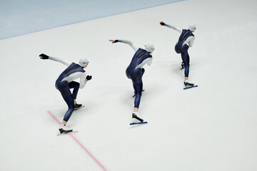 High angle of three young men in sports uniform and skates moving forwards along ice rink during...