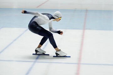 Young speed skater bending forwards over ice rink while standing or moving along arena during race...
