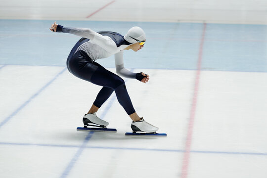 Young speed skater bending forwards over ice rink while standing or moving along arena during race or practice of new exercises