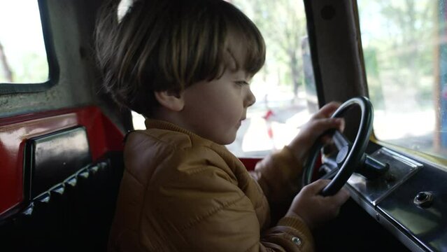 One joyful child playing with steering wheel inside car carousel at amusement park