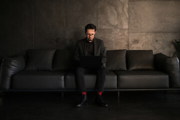 a young man in a suit sits in a stylish coworking space and works at a laptop